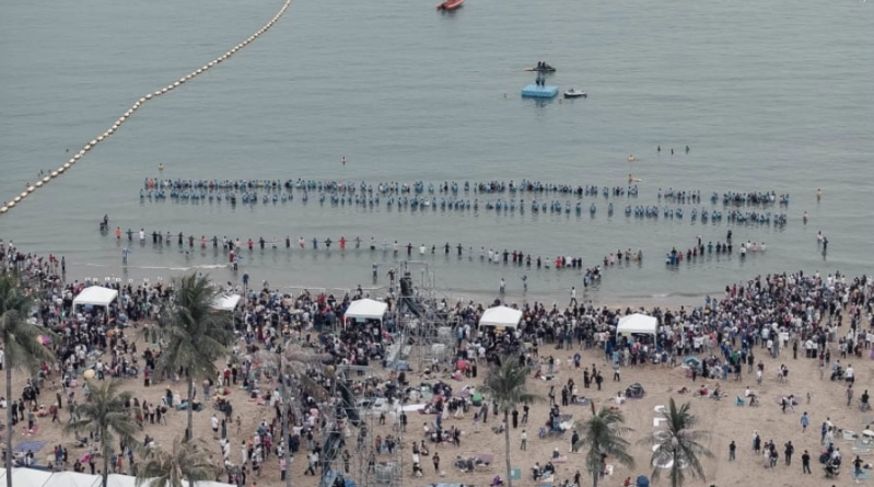 Baptism candidates hold hands, forming a unified chain as they enter the ocean